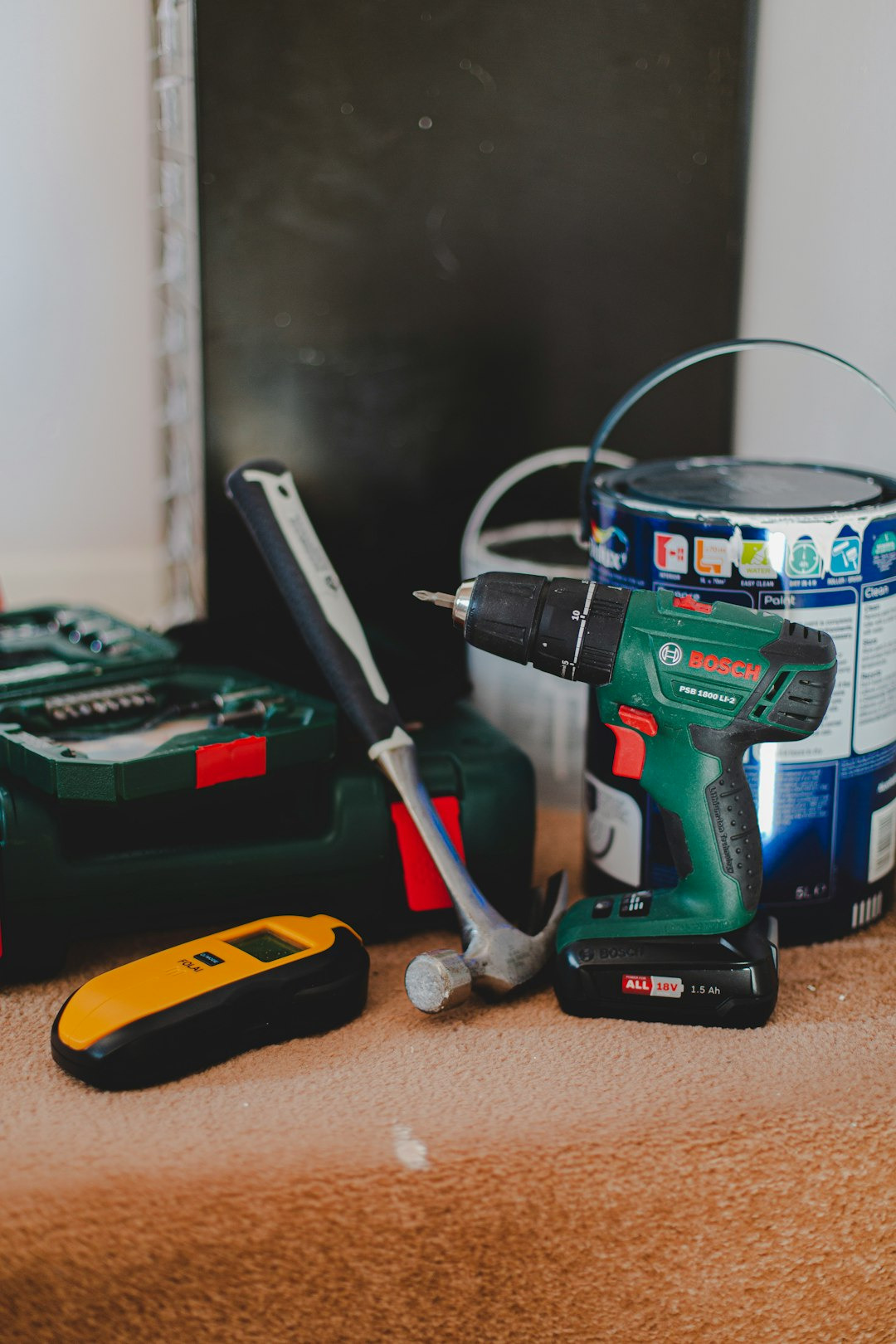 a collection of tools, a hammer, a power drill, a paint tin, a wall stud finder, a drill box